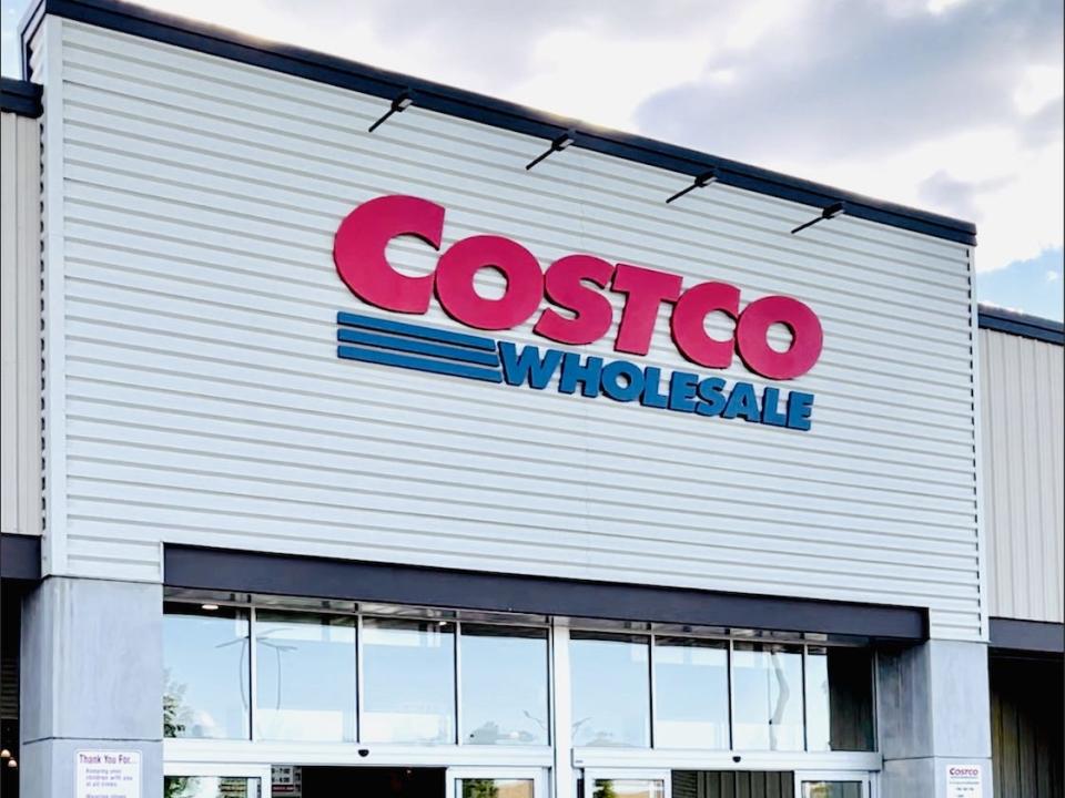 The outside of Costco with a white exterior and blue-and-red sign with the sky in the background