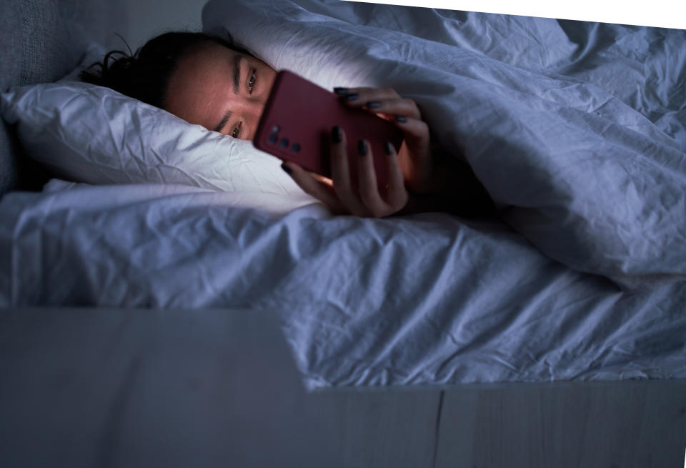 Woman lying in bed at night looking at her cell phone.