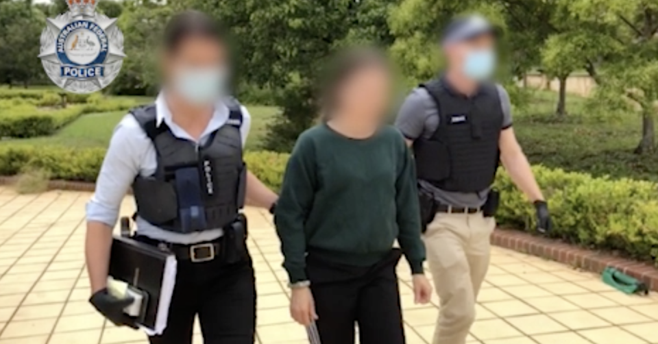 Screenshot of a woman wearing a green pull over with dark hair and black pants escorted by two police officers. Source: AFP