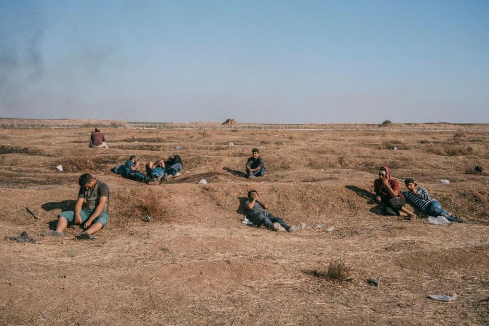 Palestinians sit along the Gaza-Israel border as smoke wafts in the distance.