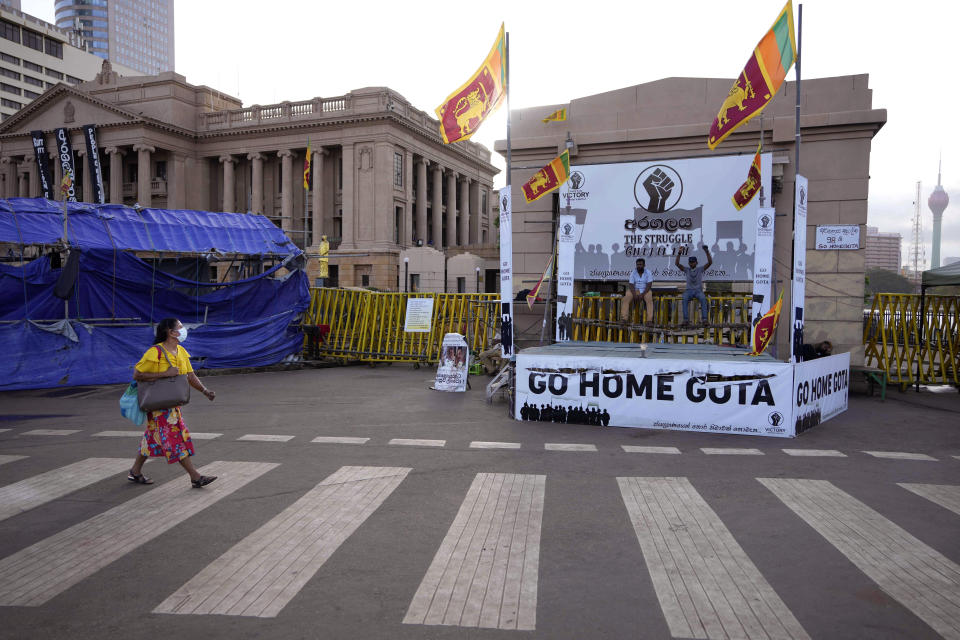 A woman walks past protesters blocking the entrance to presidential secretariat in Colombo, Sri Lanka, Friday, July 15, 2022. Protesters retreated from government buildings Thursday in Sri Lanka, restoring a tenuous calm to the economically crippled country, and the embattled president at last emailed the resignation that demonstrators have sought for months.(AP Photo/Eranga Jayawardena)