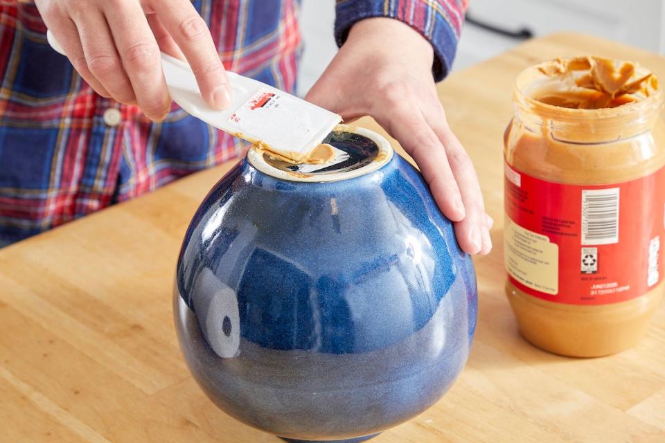 Woman spreads peanut butter on bottom of a blue vase to remove price sticker.