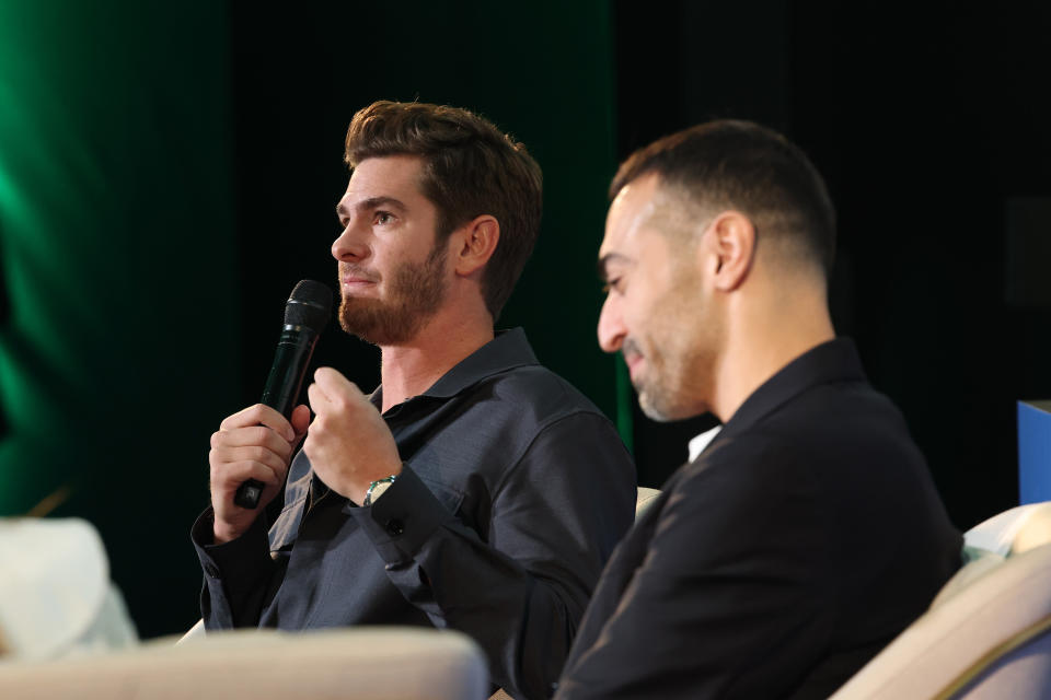 Andrew Garfield speaks into a microphone while sitting on stage