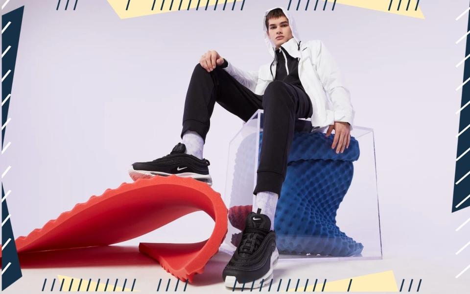 a mann sitting on a blue object with his foot on a red object wearing Nike Air Max sneakers
