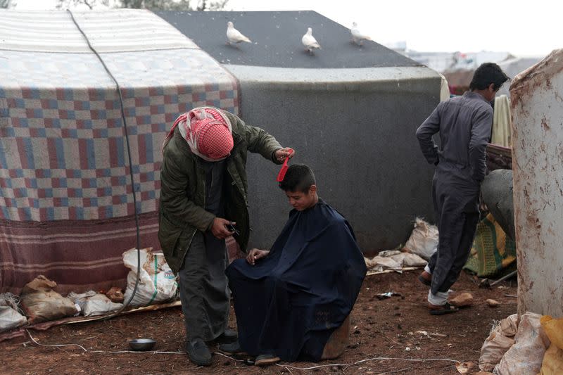 An internally displaced youth gets a haircut outside tents at a makeshift camp in Azaz