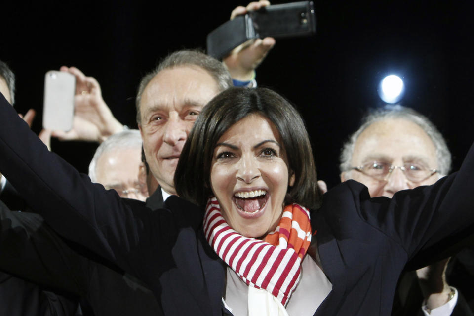 French Socialist Party deputy mayor of Paris, Anne Hidalgo, center, smiles, as outgoing mayor Bertrand Delanoe, stands behind her, during a speech after results were announced in the second round of the French municipal elections, in Paris, Sunday, March 30, 2014. Hidalgo saved Paris for the flagging Socialist Party in Sunday's municipal elections, becoming the French capital's first female mayor. (AP Photo/Thibault Camus)