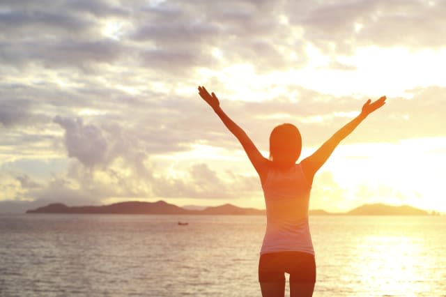 back of fitness woman open arms to sunrise at seaside