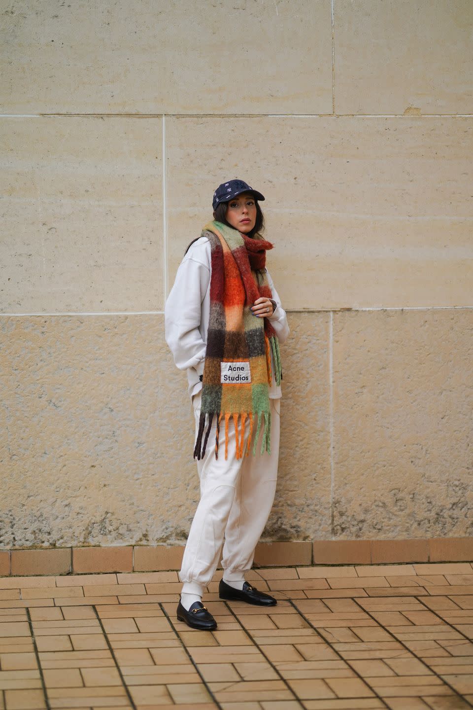 paris, france february 02 gabriella berdugo wears a calvin klein outfit made of beige sweat jogger sportswear pants and a white oversized sweat shirt, white socks, gucci black leather loafers shoes, a multi color oversized maxi wool fringed scarf from acne studios, a blue ny new era monogram cap hat, on february 02, 2021 in paris, france photo by edward berthelotgetty images