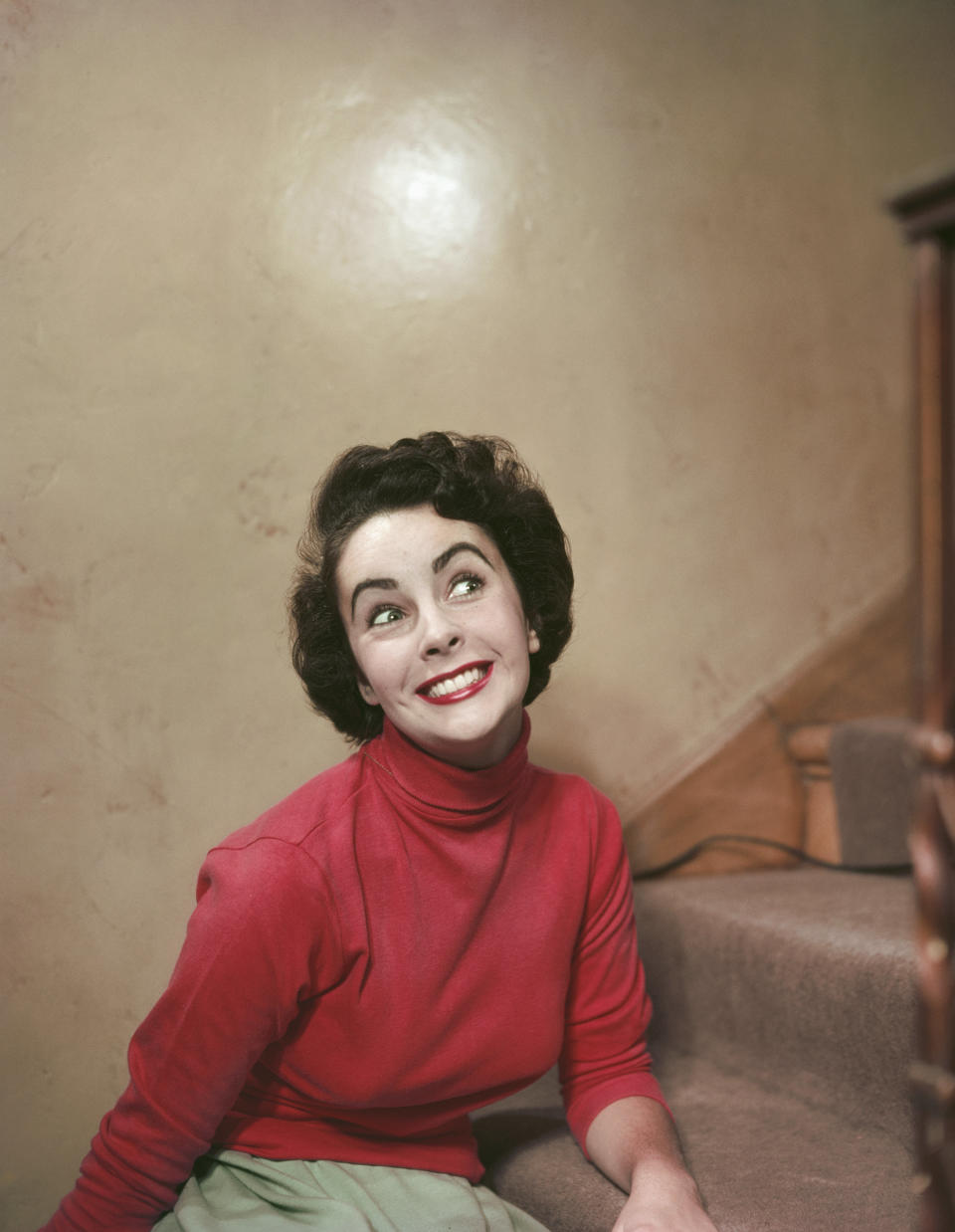The actress offers a big smile&nbsp;on a stairway in a red turtleneck, sometime in the '50s.