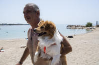 A man carries his dog during a heatwave at a beach, in Alimos suburb, southern Athens, Greece, Monday, Aug. 2, 2021. The heat wave is expected to peak Monday, with temperatures inland ranging from 42 to 46 degrees Celsius (107.6 to 114.8 Fahrenheit). Temperatures will remain at 40 Celsius (104 Fahrenheit) or above in much of Greece until at least Friday, meteorologists say. (AP Photo/Michael Varaklas)