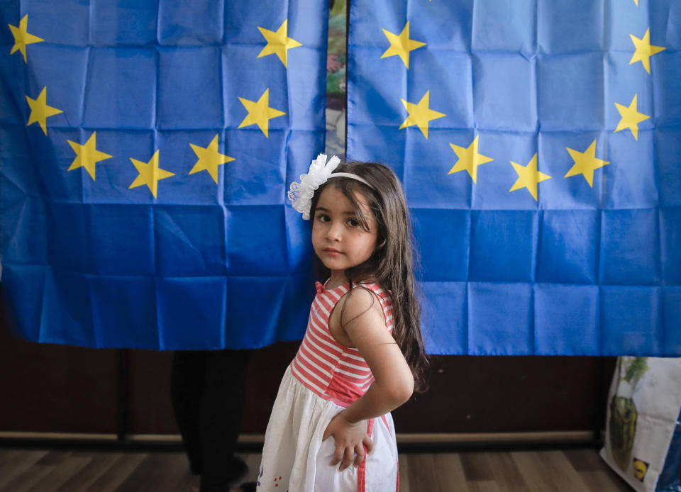 A child waits outside voting cabins with curtains depicting the European Union in Baleni, Romania, Sunday, May 26, 2019. The ruling Social Democratic Party (PSD) suffered a major blow in the European Parliament elections according to the country's only exit poll. (AP Photo/Vadim Ghirda)