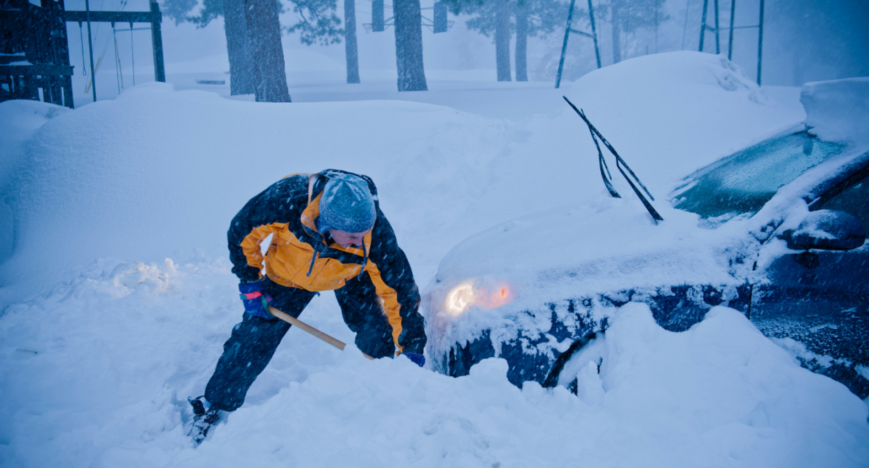 man shovelling car out of snowbank at night