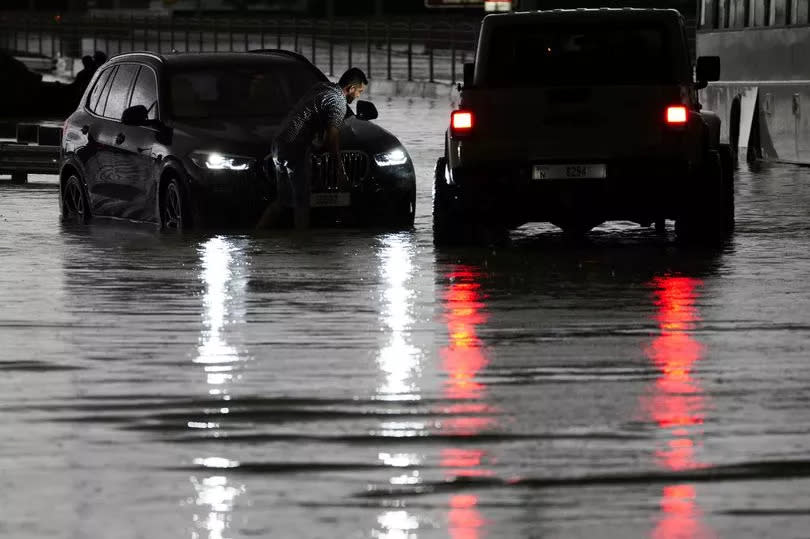 A man tries to work on his stalled SUV in standing water in Dubai, United Arab Emirates, Tuesday, April 16, 2024.