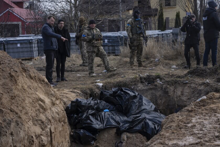 People standing next to a mass grave in Bucha, Ukraine