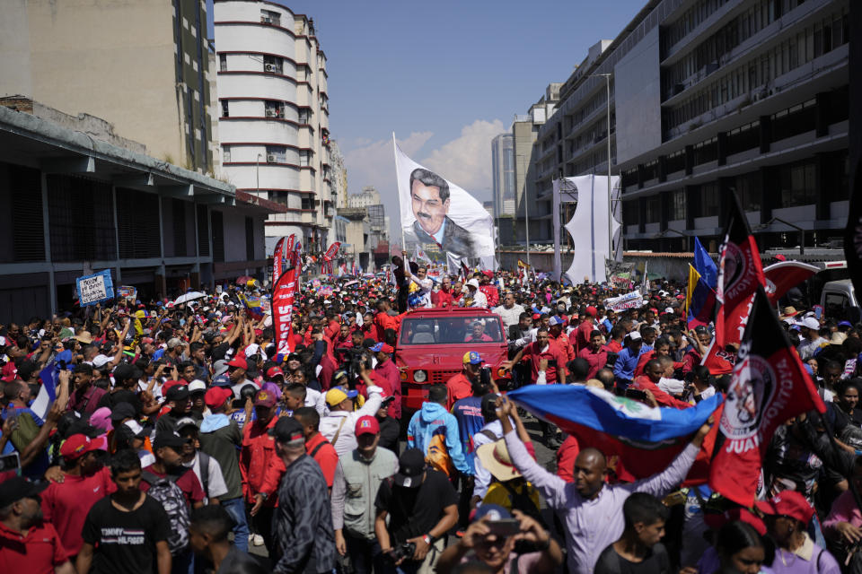 FILE - Venezuelan President Nicolas Maduro waving a banner emblazoned with an image of himself is accompanied by supporters as he is driven to the electoral council headquarters to register his candidacy for a third term, in Caracas, Venezuela, March 25, 2024. (AP Photo/Matias Delacroix, File)