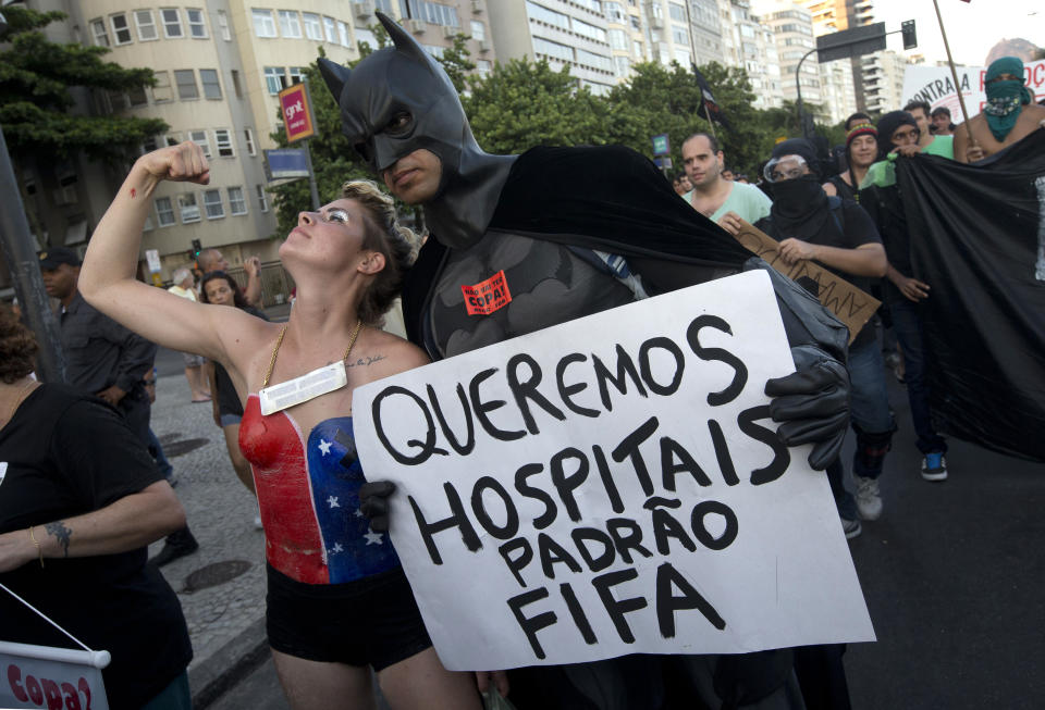 A man dressed as Batman holds a sign that reads in Portuguese "We want FIFA quality hospitals " as a woman in a super hero costume flexes her muscles at a protest demanding better public services in Rio de Janeiro, Brazil, Saturday, Jan. 25, 2014. Last year, millions of people took to the streets across Brazil complaining of higher bus fares, poor public services and corruption while the country spends billions on the World Cup, which is scheduled to start in June. (AP Photo/Silvia Izquierdo)