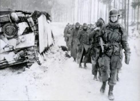 A paratrooper of the 82nd Airborne Division leads a column of German prisoners past a disabled German tank during the Battle of the Bulge.