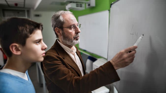 Senior teacher teaching high school student on a blackboard.