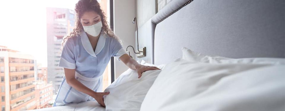 Maid working at a hotel and doing the bed wearing a facemask