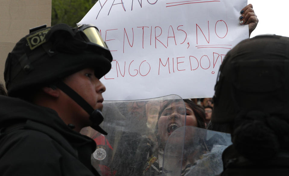 A supporter of opposition presidential candidate Carlos Mesa, a former president, yells holding the Spanish sign "No more lies. I'm not scared!" as police stand guard outside the Supreme Electoral Court where election ballots are being counted in La Paz, Bolivia, Monday, Oct. 21, 2019. A sudden halt in release of presidential election returns led to confusion and protests in Bolivia on Monday as opponents suggested officials were trying to help President Evo Morales avoid a risky runoff. (AP Photo/Juan Karita)