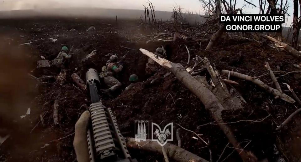 Bodycam footage shows the barrel of a rifle, pointing out over four Ukranian soldiers crouching in an earth mound they are defending from attack.