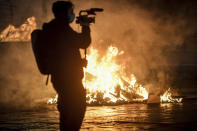 A cameraman films fire after clashes broke out during a protest against the government restriction measures to curb the spread of COVID-19 in Turin, Italy, Monday, Oct. 26, 2020. Protesters turned out by the hundreds in Italian several cities and towns on Monday to vent anger, sometimes violently, over the latest anti-COVID-19 rules, which force restaurants and cafes to close early, shutter cinema, gyms and other leisure venues. In the northern city of Turin, demonstrators broke off from a peaceful protest and hurled smoke bombs and bottles at police in the city square where the Piedmont regional government is headquartered. (Claudio Furlan/LaPresse via AP)