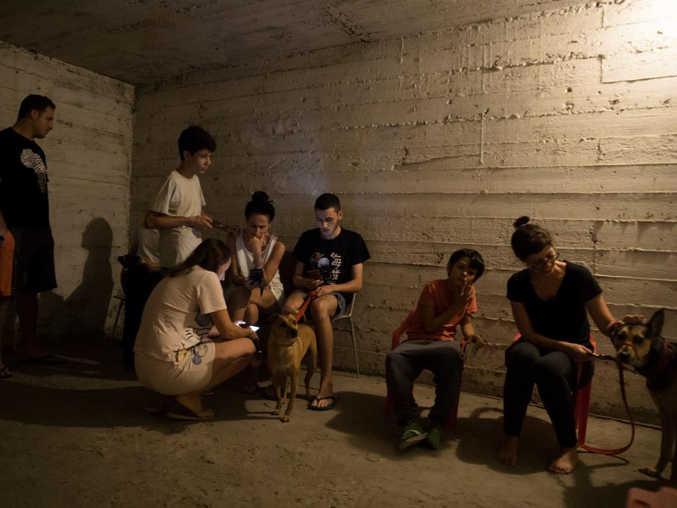 A group of eight people and two dogs take refuge in a concrete bomb shelter in Israel.
