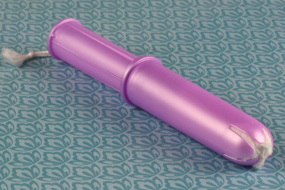 Purple tampon with an applicator on a patterned background