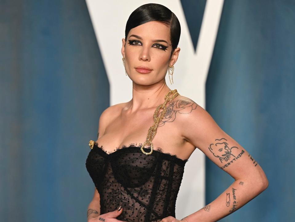 Halsey wears a black dress standing in front of a blue backdrop at the 2022 Vanity Fair Oscar Party.