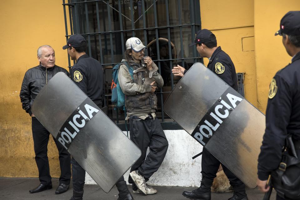 Varios policías antimotines caminan frente a un hombre con un gato cerca del Palacio Legislativo en Lima, Perú, el miércoles 19 de septiembre de 2018. Los legisladores peruanos debatían el llamado del presidente Martín Vizcarra a un referéndum sobre medidas anticorrupción. Si el Congreso se niega a respaldar su plan, entonces Vizcarra tendrá el poder de disolver la legislatura, algo que no ha ocurrido desde el gobierno autoritario de Alberto Fujimori en 1992. (AP Foto/Rodrigo Abd)