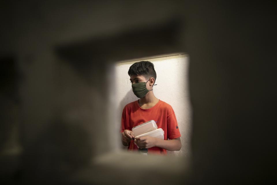 A boy wearing a face mask to avoid the spread of the new coronavirus waits outside of an apartment with his containers to be filled with food at a soup kitchen in Caracas, Venezuela, Thursday, April 9, 2020. The food is donated by the organization "Feeds Solidarity" every week, and feeds 60 children. (AP Photo/Ariana Cubillos)