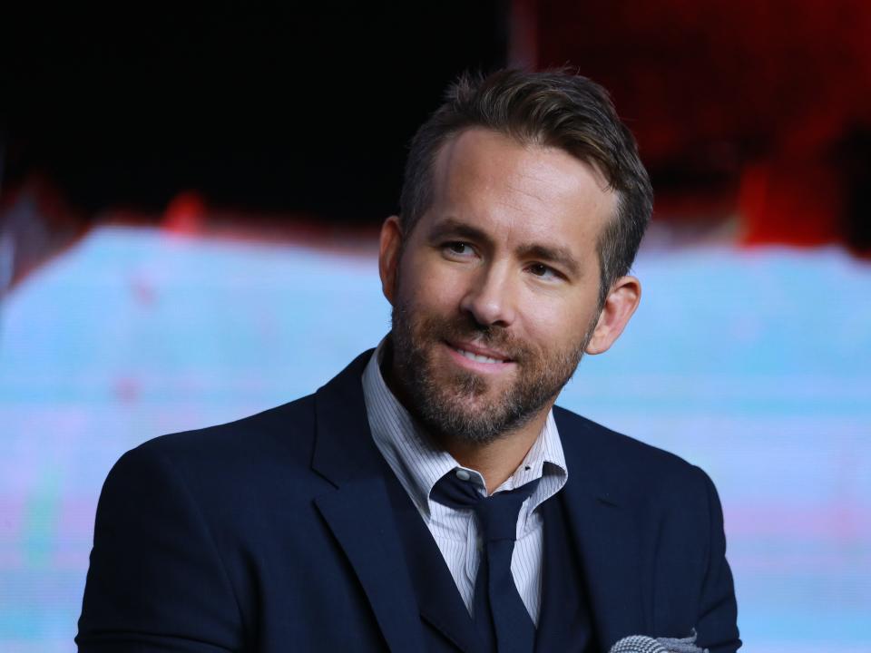 Ryan Reynolds in a navy blue suit jacket and tie with a light blue shirt