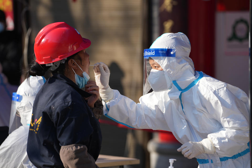In this photo released by China's Xinhua News Agency, a worker wearing a protective suit collects a throat swab sample at a COVID-19 testing site in Xi'an in northwestern China's Shaanxi Province, Tuesday, Dec. 21, 2021. China on Wednesday ordered millions of people locked down in neighborhoods and workplaces in the northern city of Xi'an following a spike in coronavirus cases. (Li Yibo/Xinhua via AP)