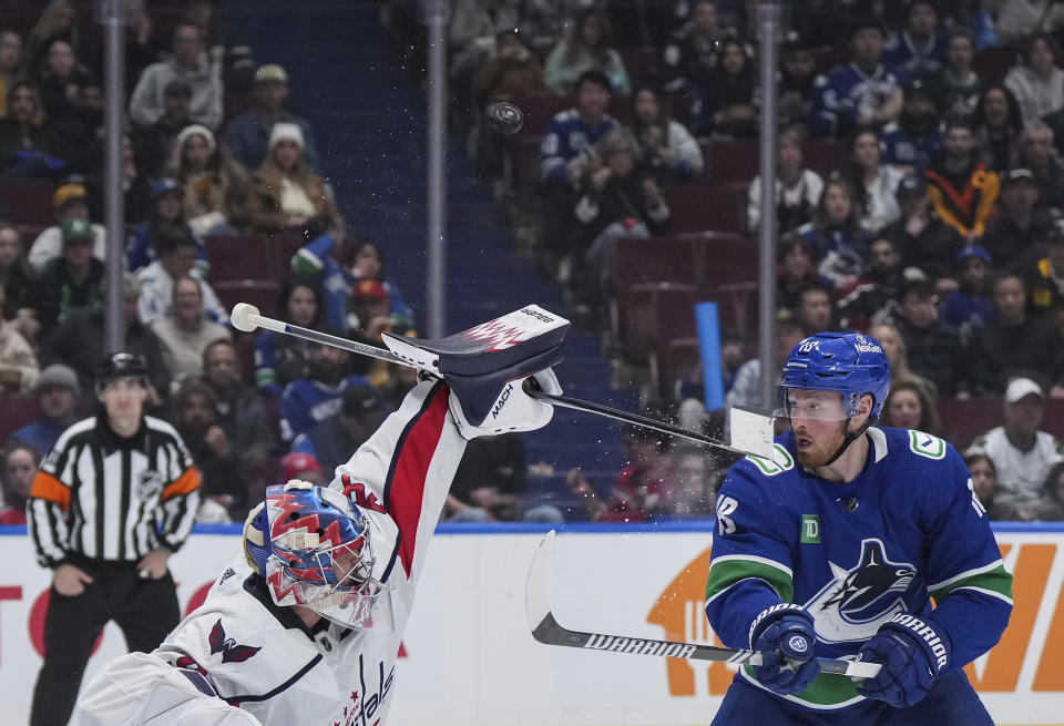 Washington Capitals goalie Charlie Lindgren, left, makes a blocker save and strikes Vancouver Canucks' Sam Lafferty in the face with his stick during the third period of an NHL hockey game in Vancouver, British Columbia, Saturday, March 16, 2024. (Darryl Dyck/The Canadian Press via AP)