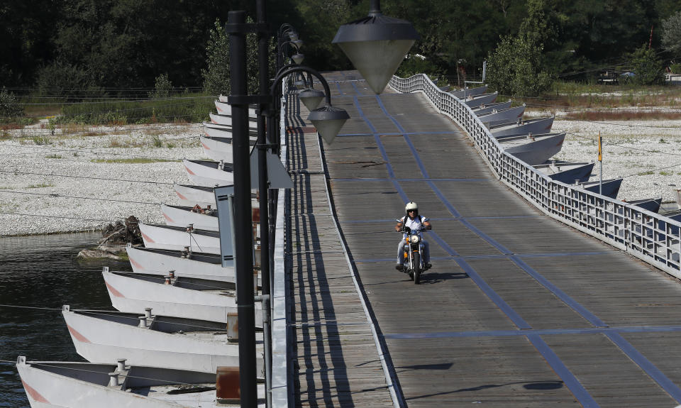 A man rides his motorbike on a "Ponte delle Barche" bridge on the Ticino river in Bereguardo, near Pavia, Italy, Friday, Aug. 3, 2018. Hot air from Africa is bringing a heat wave to Europe, prompting health warnings about Sahara Desert dust and exceptionally high temperatures that could peak at 47 degrees Celsius (117 Fahrenheit). (AP Photo/Antonio Calanni)