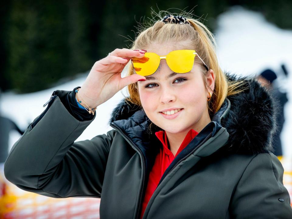 Princess Amalia of The Netherlands stands in a snowy backdrop and raises her sunglasses.