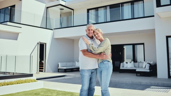 A retiring couple stands in front of the home they recently sold to downsize in retirement.