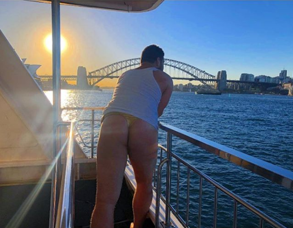 A photo of Brendan Fevola on a boat wearing a white singlet and a gold g-string.