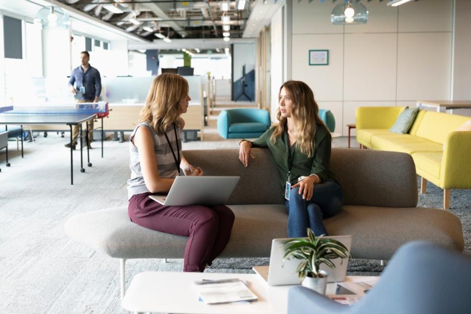 Two women in an office have a conversation on a sofa