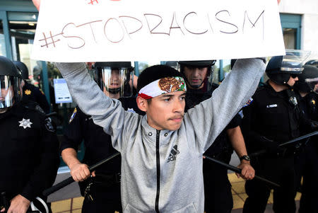 A protester holds up a sign in front of police in riot gear as he and fellow protesters demonstrate against Donald Trump outside the Hyatt hotel where Trump is speaking at the California GOP convention in Burlingame, California April 29, 2016. REUTERS/Noah Berger