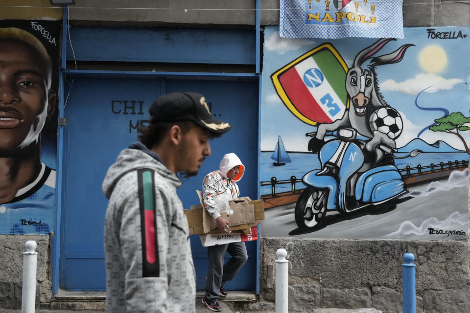 People walk past murals of Napoli soccer team striker Victor Osimhen, left and the team mascot in Naples, Italy, Monday, May 1, 2023. Napoli wasted what seemed like a perfect chance to seal the Serie A title, at home inside the Stadio Diego Armando Maradona on a holiday weekend afternoon in a 1-1 draw with regional rival Salernitana on Sunday. The result disappointed legions of Napoli fans who had already started celebrating in anticipation of the championship. (AP Photo/Gregorio Borgia)