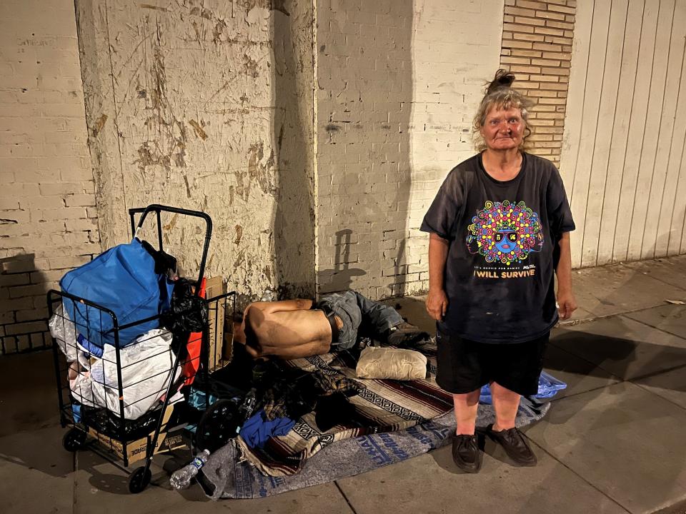 Kathy Shows, 63, stands beside her resting place for the night near downtown Phoenix. She and her boyfriend, Fernando, sleeping behind her, are unhoused and struggled to find adequate shelter from extreme temperatures during the July 2023 record-setting heat wave.
