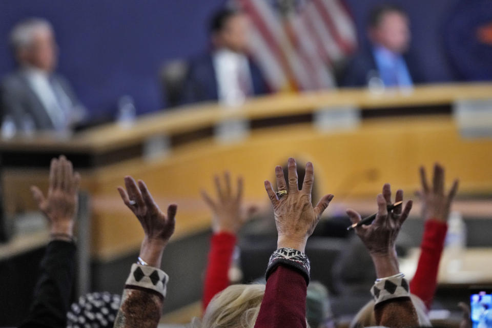 People wave their hands in protest during the Maricopa County Board of Supervisors during their general election canvass meeting, Nov. 28, 2022, in Phoenix. Officials in several presidential battleground states are proposing to increase spending to hire more election staff, improve security and expand training ahead of the 2024 election. The proposed funding increases come as many election offices are grappling with a wave of retirements and a flood of public records requests from election skeptics. (AP Photo/Matt York)