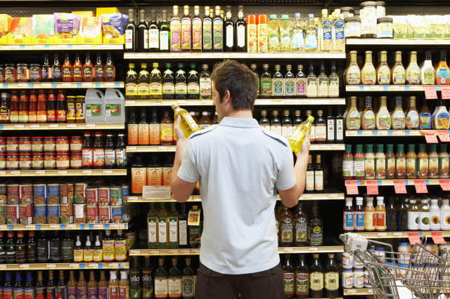 Young man in supermarket comparing bottles of oil, rear view, close-up