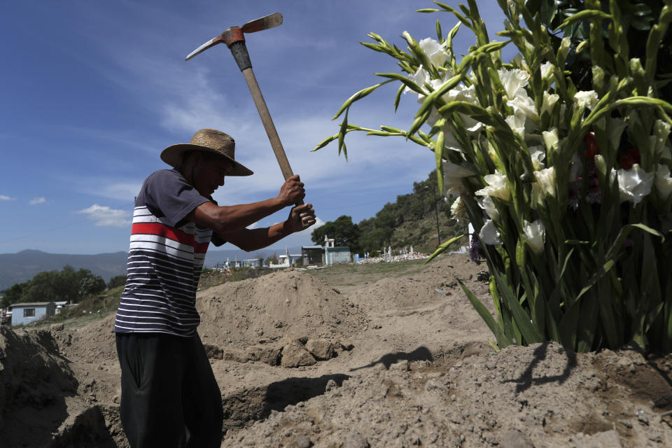 Worker Martin Niano uses a pick to dig a grave in a new section of the Municipal Cemetery of Valle de Chalco opened two months ago to accommodate the surge in deaths amid the ongoing coronavirus pandemic, on the outskirts of Mexico City, Thursday, July 2, 2020. (AP Photo/Rebecca Blackwell)