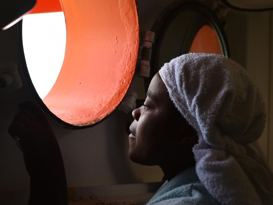 A woman looks through a window of rescue ship 'Aquarius' as more the 380 migrants arrive in the port of Cagliari, Sardinia, on May 26, 2016, two days after being rescued near the Libyan coasts.&nbsp;