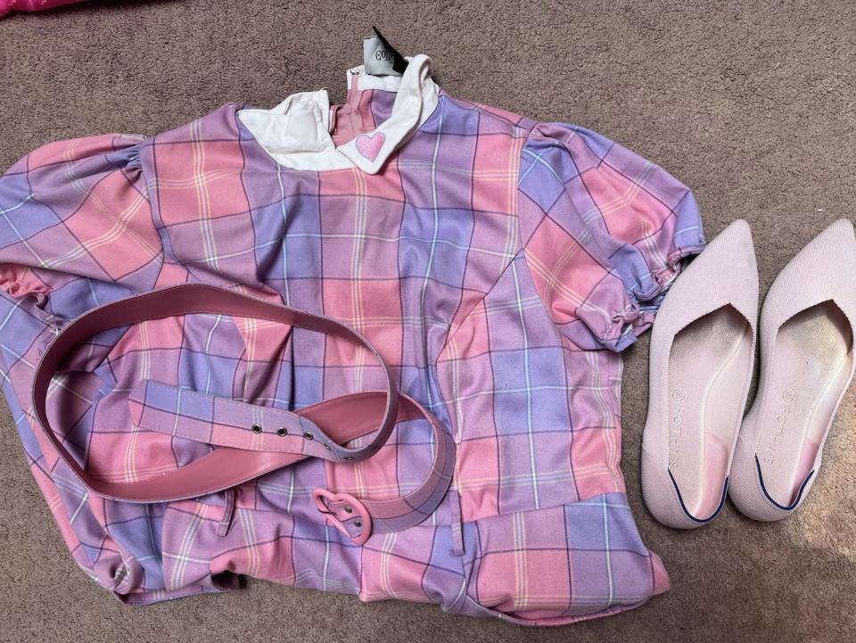 a pink and purple plaid dress folded on the floor next to light pink pointed flats and a belt