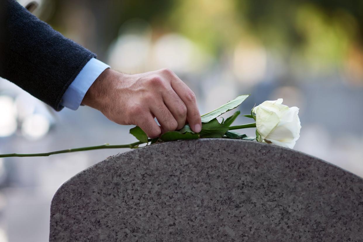 Man putting a white flower on a gravestone