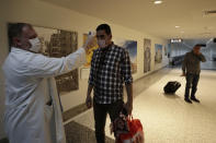 FILE - In this March 9, 2020 file photo, a passenger has his temperature checked as a precaution against a new coronavirus upon his arrival at the Rafik Hariri International Airport in Beirut, Lebanon. On Wednesday, July 1, 2020, Beirut's airport is partially reopening after a three-month shutdown and Lebanon's cash-strapped government hopes thousands of Lebanese expatriates will return for the summer, injecting badly needed dollars into the sinking economy. (AP Photo/Hassan Ammar, File)