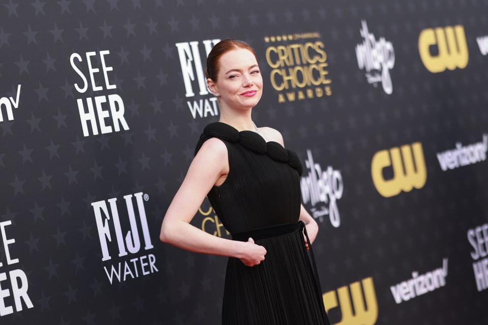 emma stone holding her hands against her hips while turning to the right and smiling on the critics choice awards red carpet